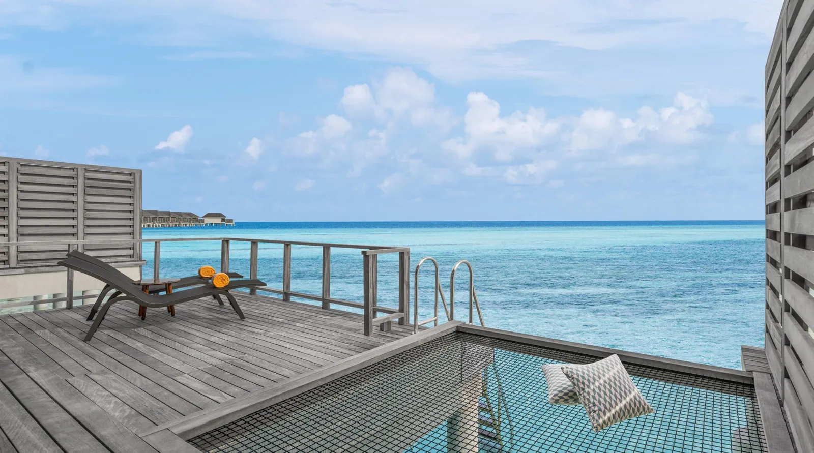 A Sunrise Overwater Villa’s deck, a lounger and the net hammock over the lagoon