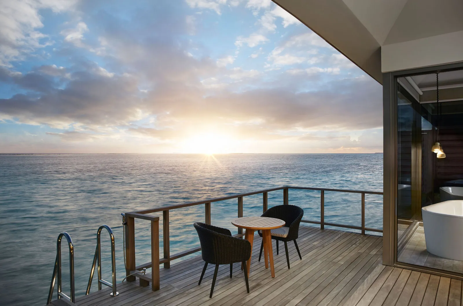 A Sunset Overwater Villa’s bedroom open to the deck, at sunset