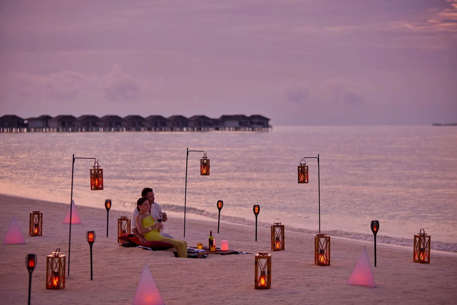 Dinner on the beach at sunset, the couple seated among lanterns and torches