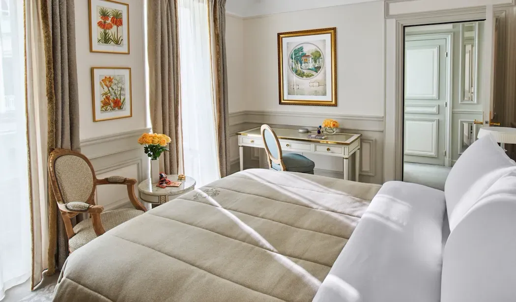 Classic Room at Le Meurice, with a bed, cream writing desk and armchair beside a tall window