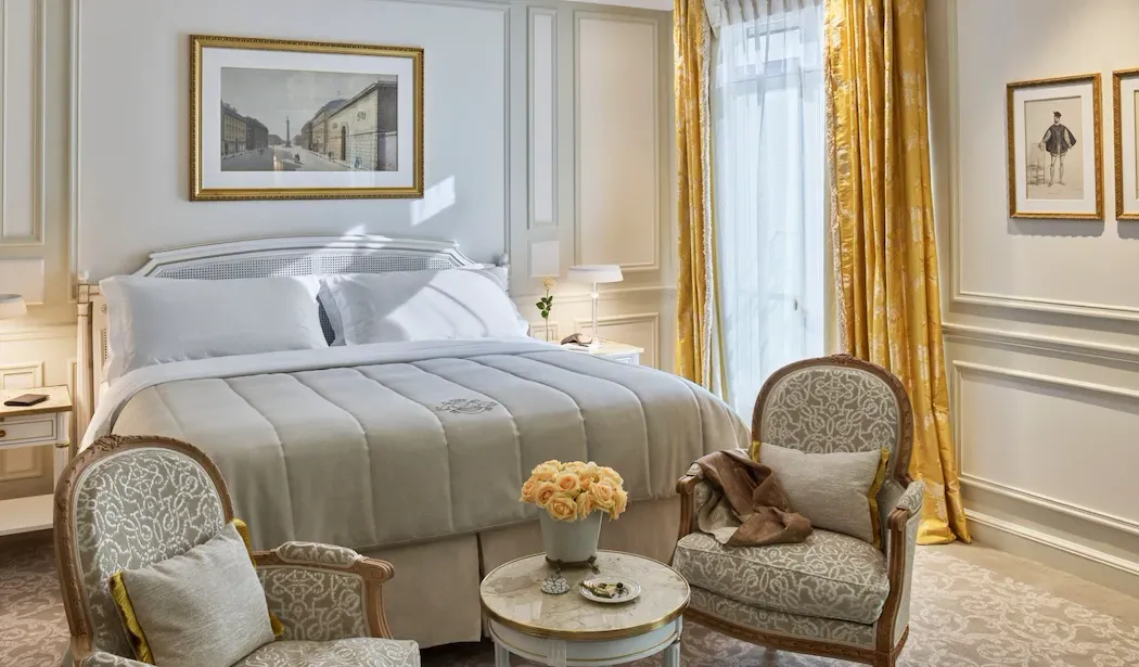 Executive Room at Le Meurice, with yellow curtains and 2 armchairs around a small table at the foot of the bed