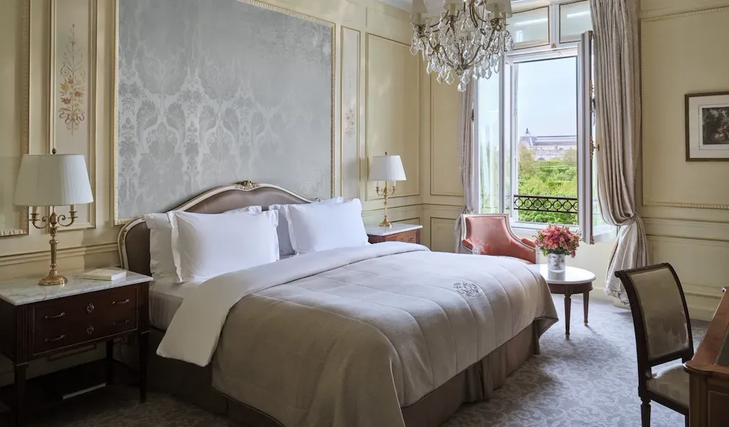 Heritage Suite, Park View at Le Meurice, with a bed beneath patterned wall panels and a pink armchair beside the window