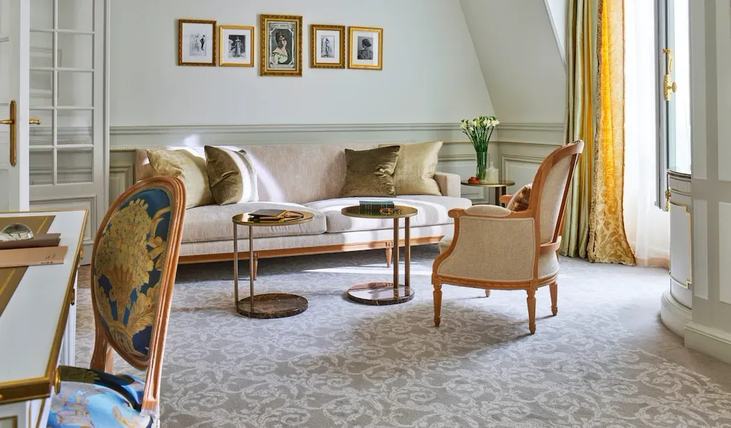 Junior Suite at Le Meurice, with a pale sofa, 2 small tables and an armchair beside a curtained window