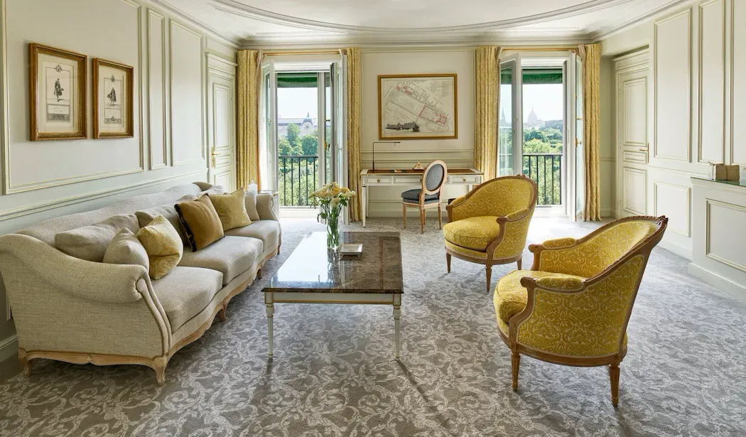 Prestige Suite, Eiffel View at Le Meurice, with a cream sofa, yellow armchairs and tall windows overlooking trees
