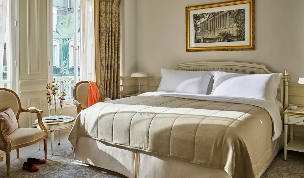 Superior Room at Le Meurice, with a bed, 2 armchairs and flowers on a small table beside the window