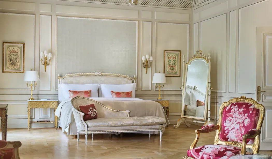 Versailles Suite, Park View at Le Meurice, with a bed behind a chaise longue, a floral armchair and a gilded mirror