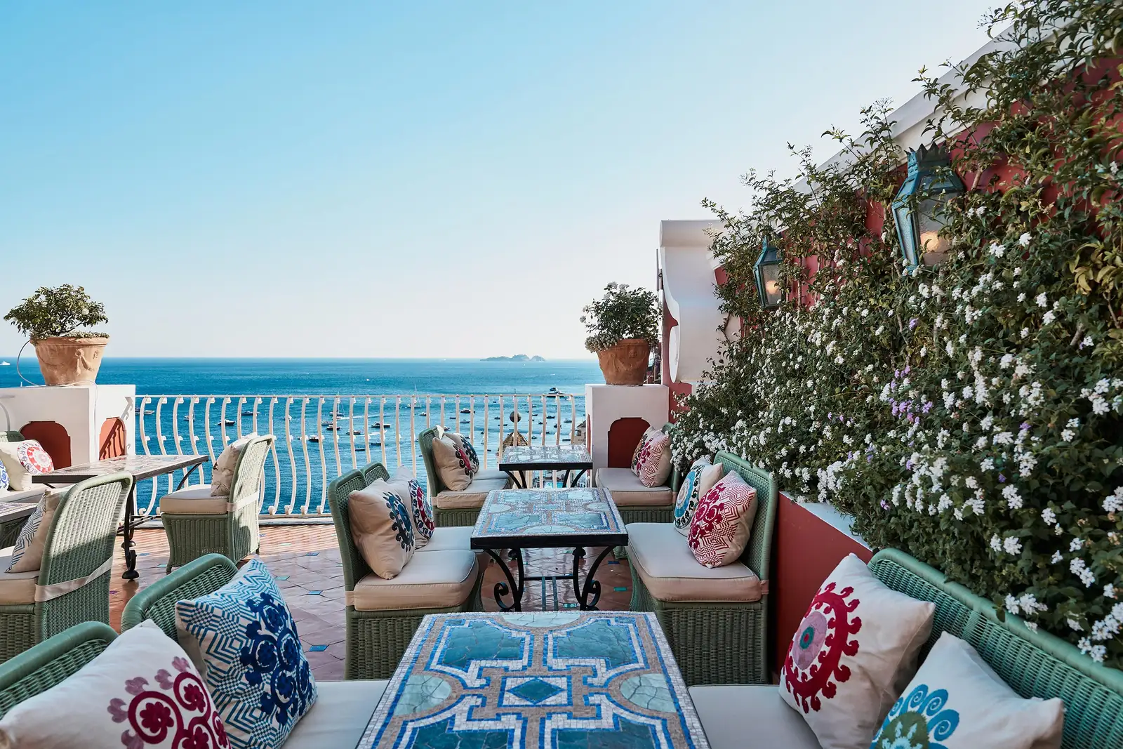 An open-air lounge at Aldo’s, with embroidered cushions, a majolica table, flowering jasmine and the sea.