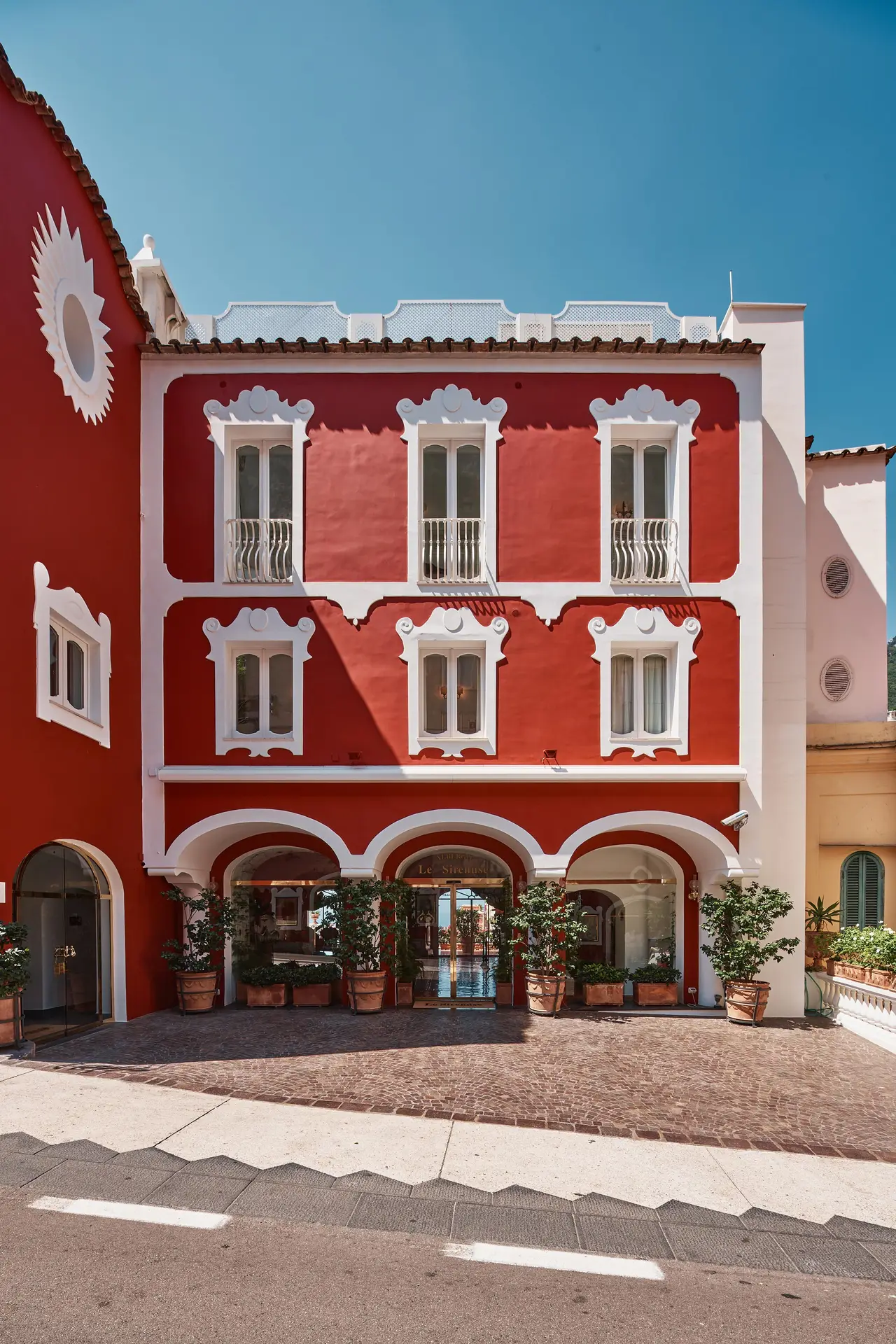 The hotel’s red façade on Via Cristoforo Colombo, with its white windows and the arches of the entrance.