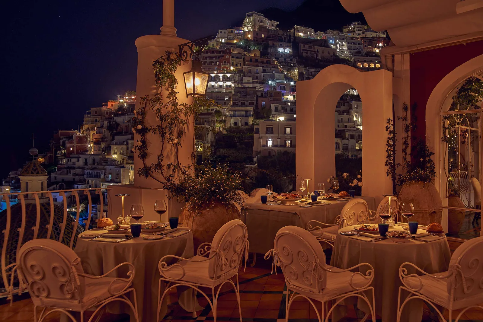 La Sponda at night, its tables laid under the arches and the lights of Positano on the hillside beyond the windows.