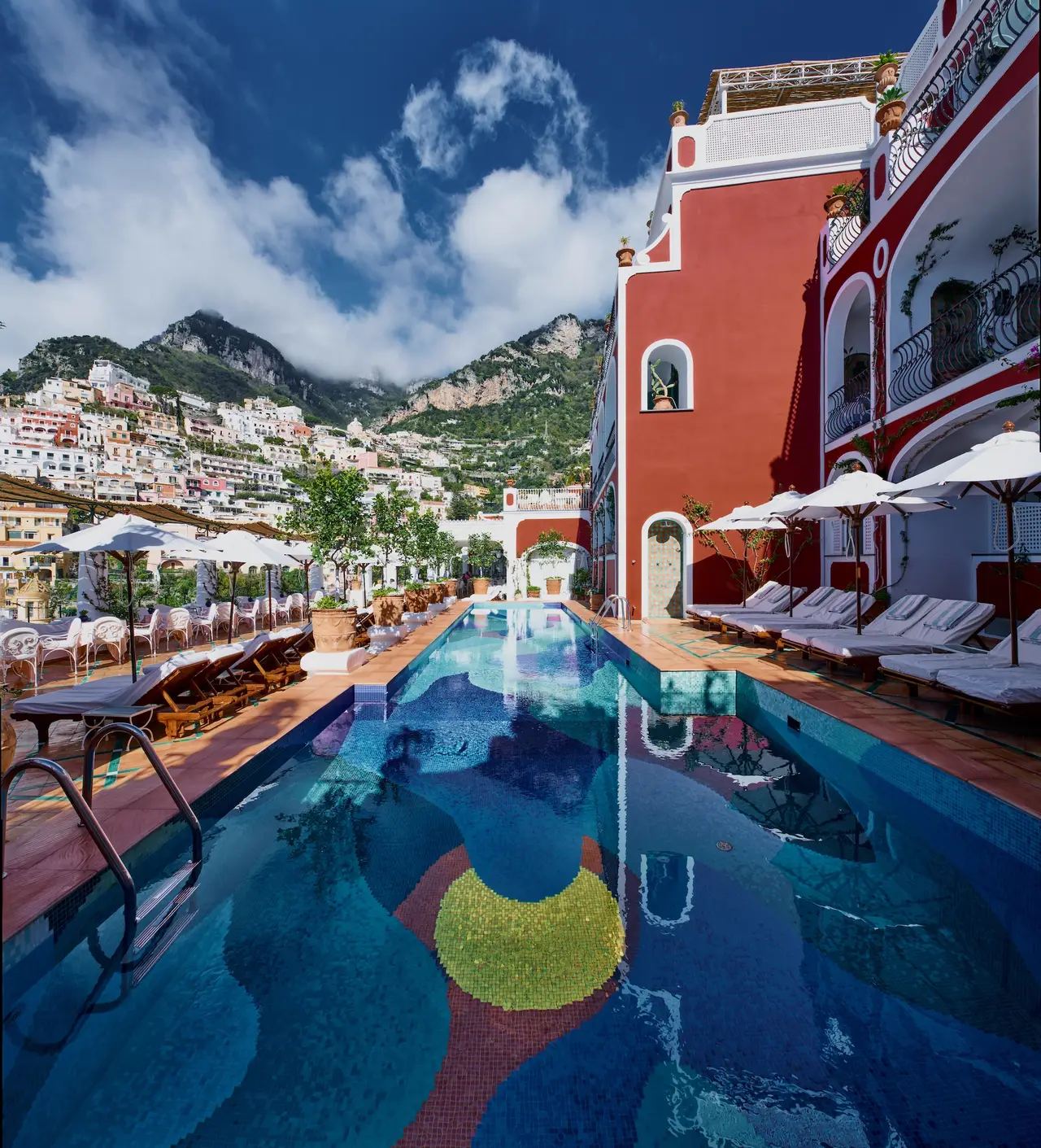 The pool with its mosaic, the red hotel on the right and the houses of Positano on the mountainside, under the clouds.