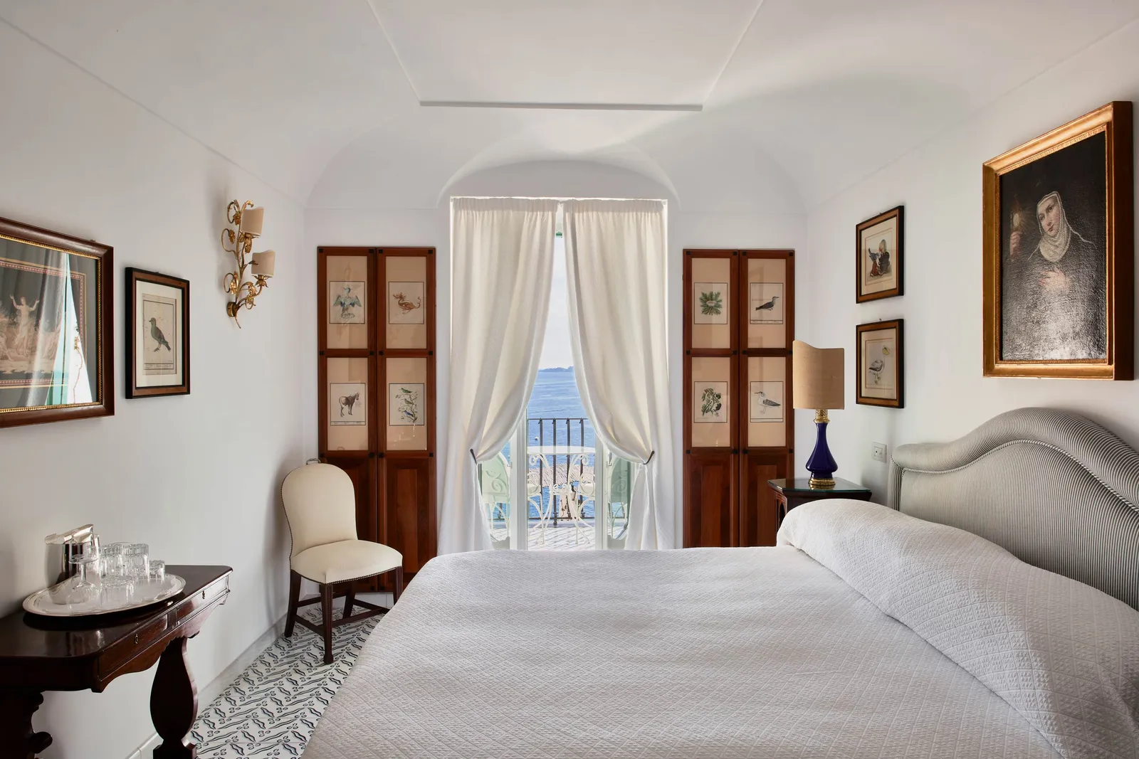A Classic Sea View room: the bed, 2 wooden cabinets and the French window between white curtains.