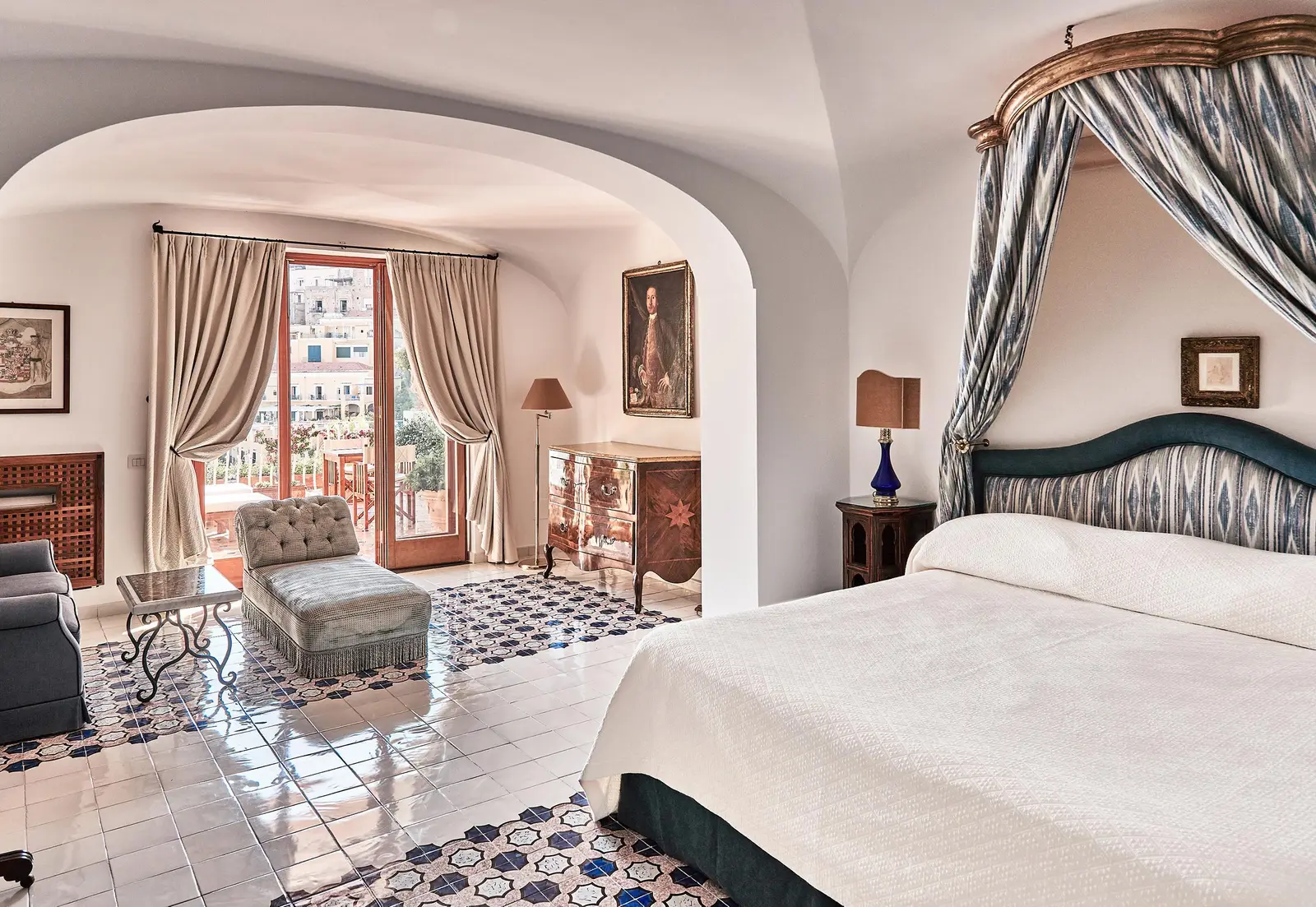 A Junior Suite Sea View: the canopy bed, the sitting area under the arch and the door open to the village.