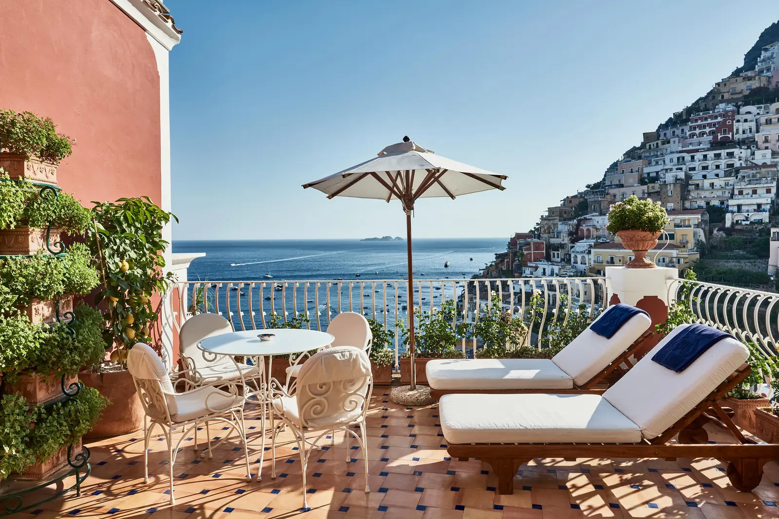 A Junior Suite Superior terrace: 2 loungers, a parasol, a table with white chairs and Positano above the sea.