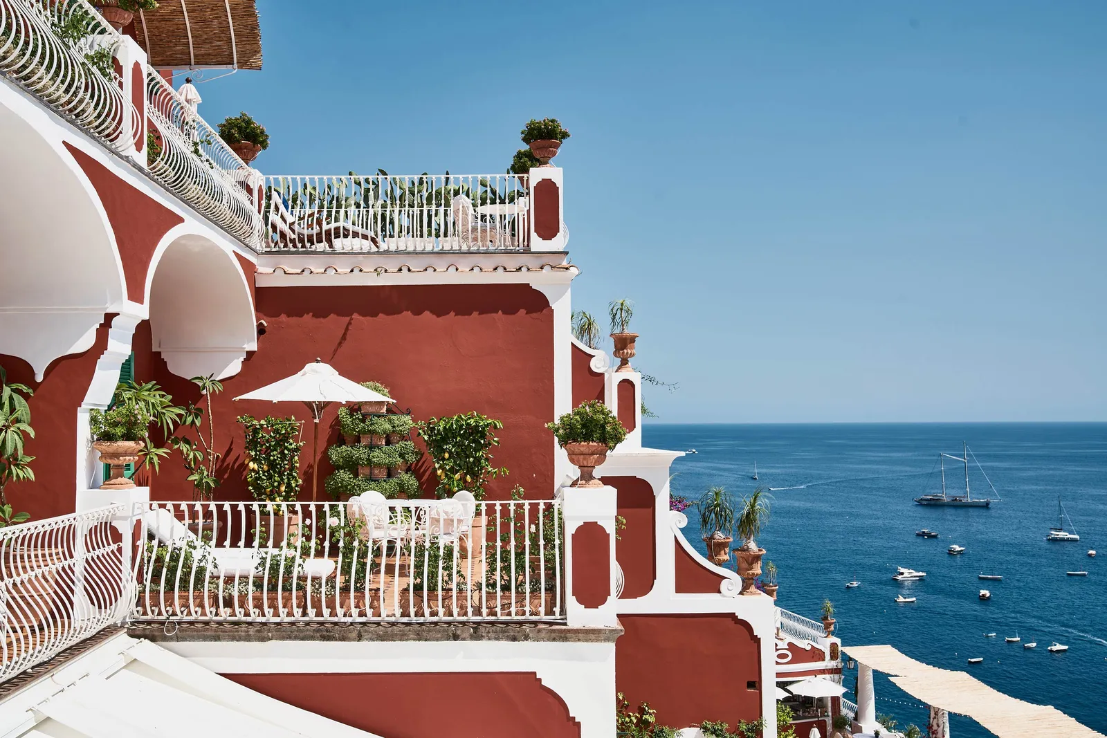 A One Bedroom Suite terrace, between the hotel’s red walls, with its white railing and boats on the sea.
