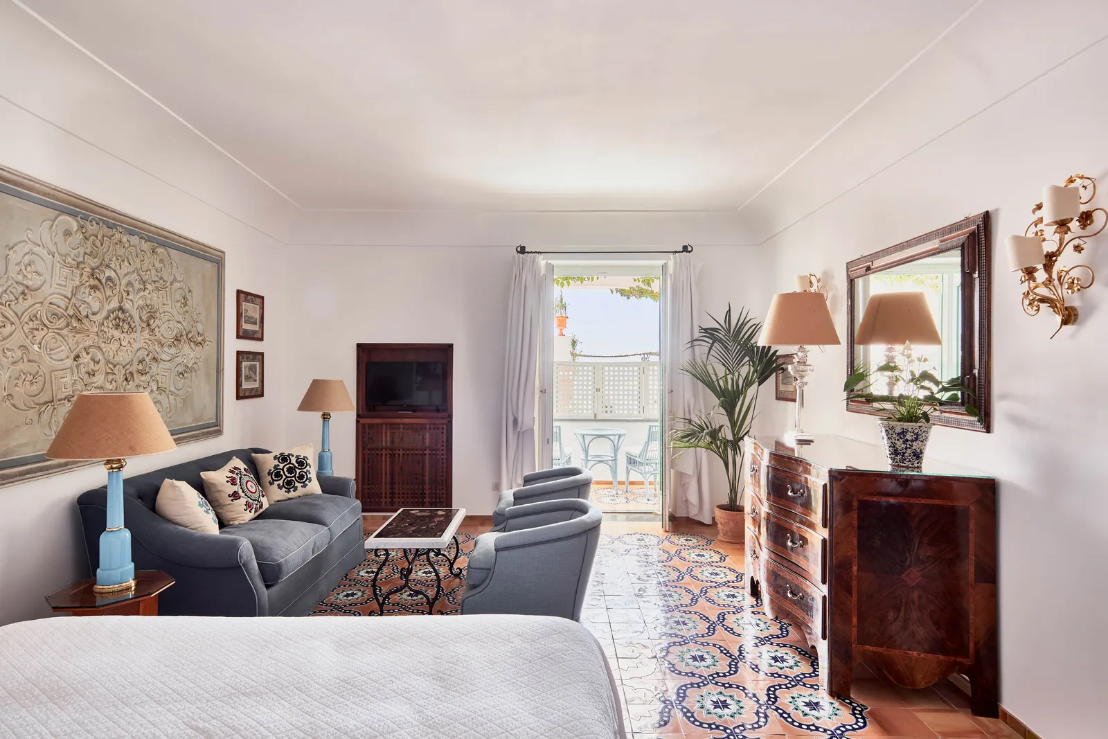 A Pool Terrace View room: the sofa, an antique chest of drawers, the majolica floor and the French window onto the balcony.