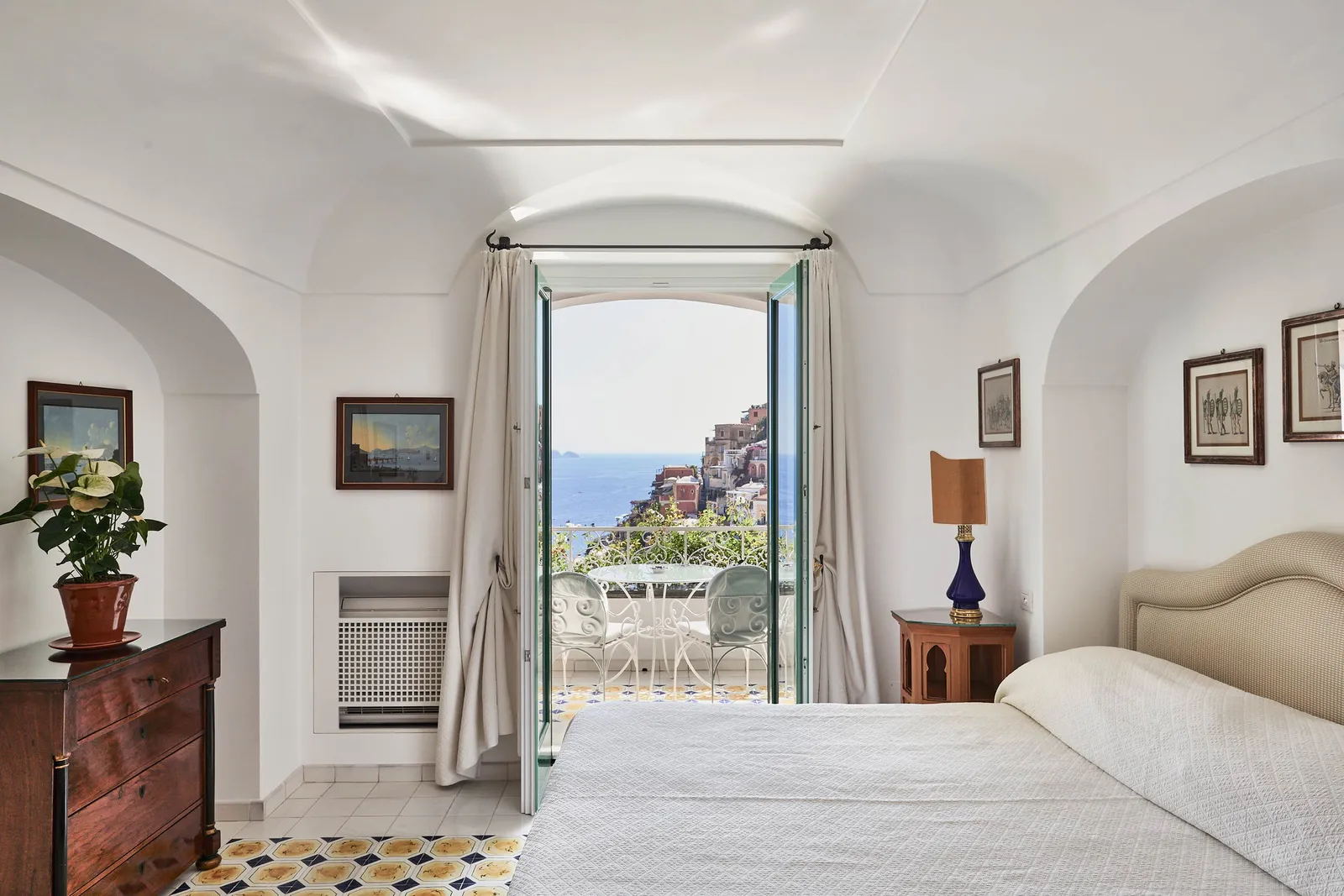 A Superior Sea View room: the bed under the white vault and the door open onto the balcony and the houses of Positano.