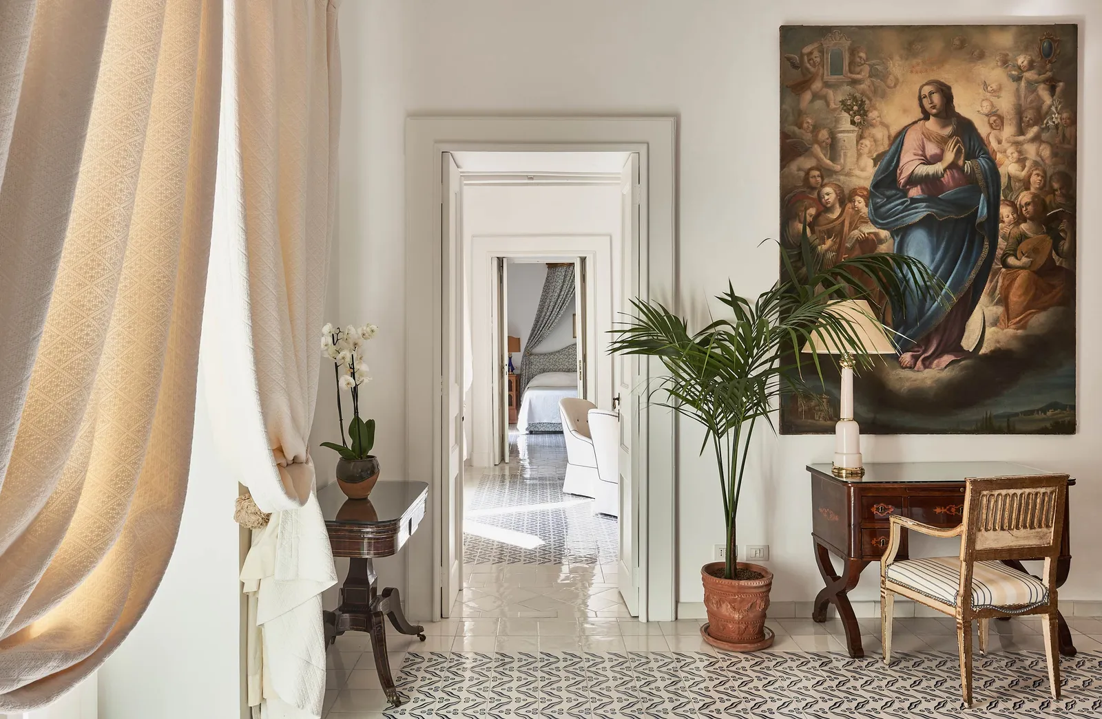 The Two Bedroom Suite’s living room: a large altarpiece, plants, a writing table and the doors through to the bedrooms.