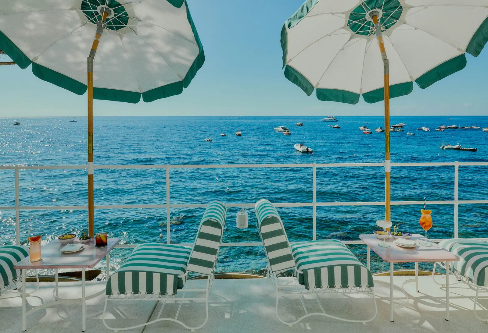 Le Sirenuse Mare at Nerano: green and white striped parasols, deckchairs on the terrace and boats in the bay.