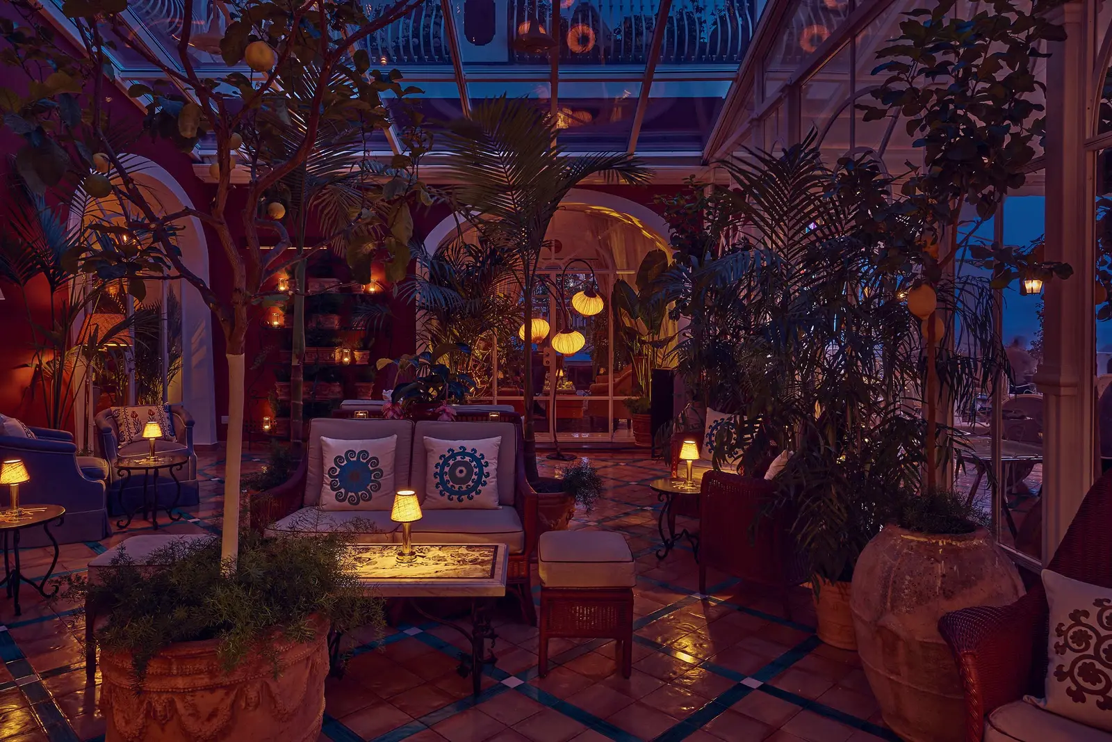 The solarium at night: low sofas, lit lamps, potted plants and the vault behind.