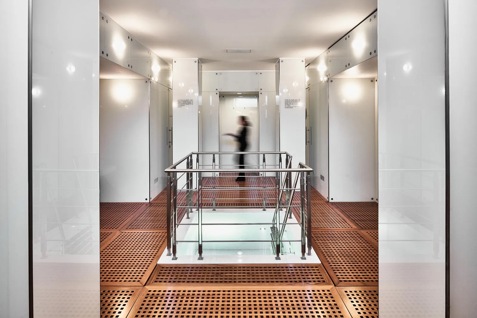The spa corridor: the teak floor, glass and steel walls and the staircase with its metal railing.
