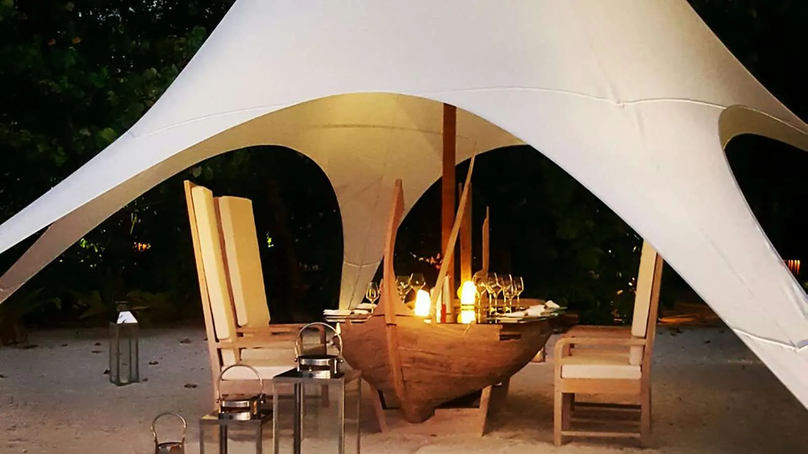 A private dinner on the beach under a white sail, among candles