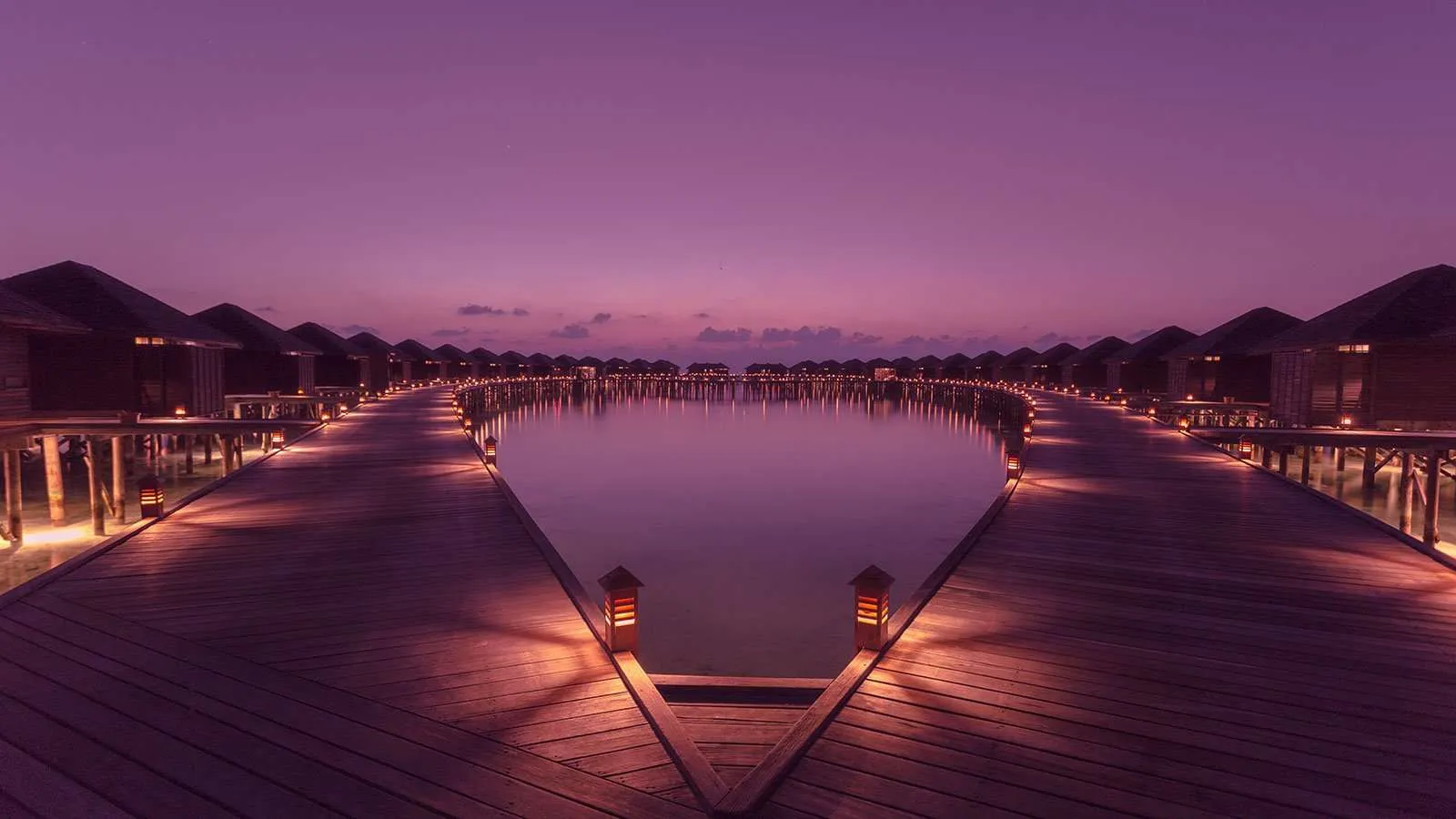 The water-villa jetty at dusk, its lights on