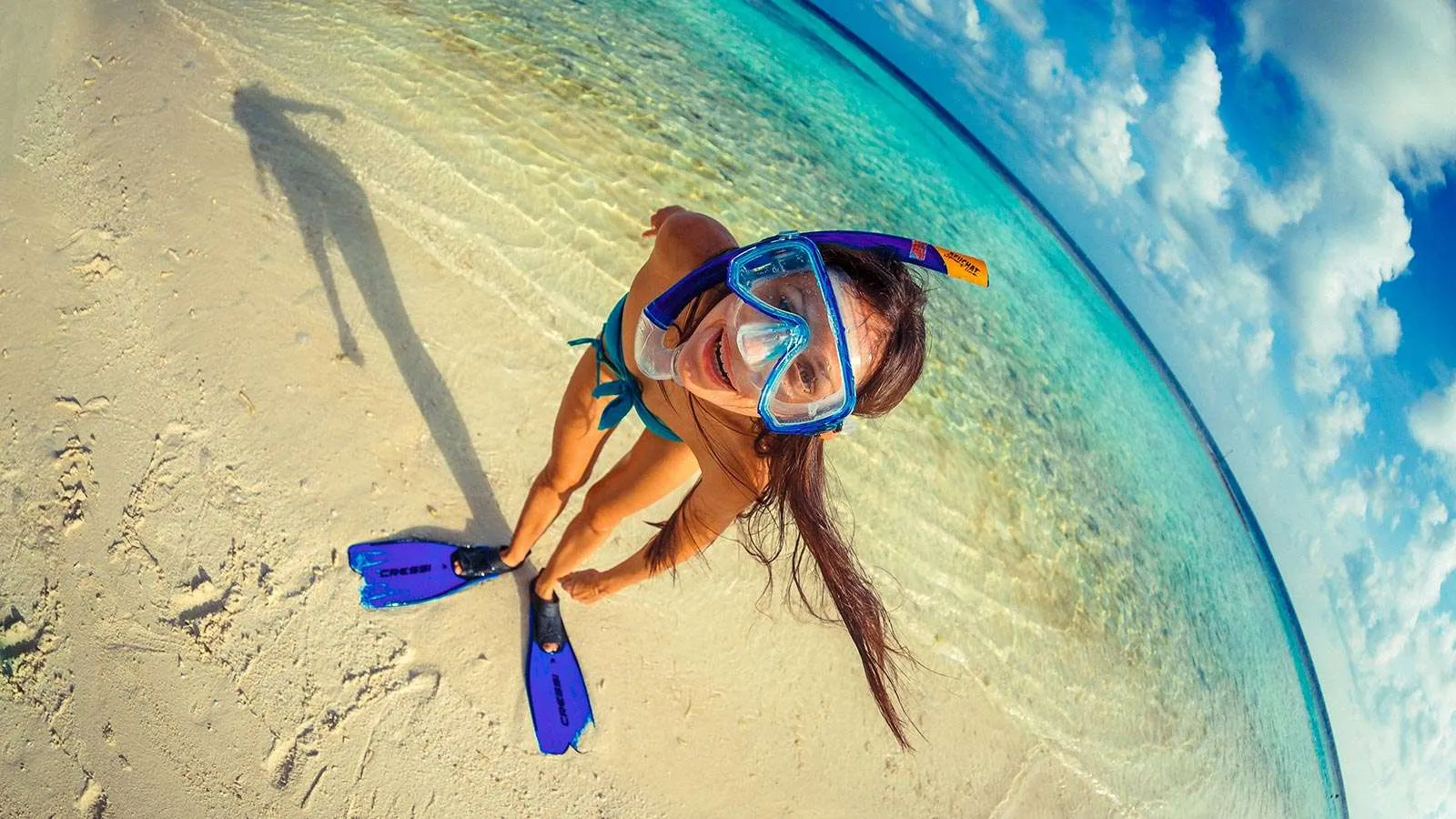 A girl in mask and fins sitting at the water’s edge, seen from above