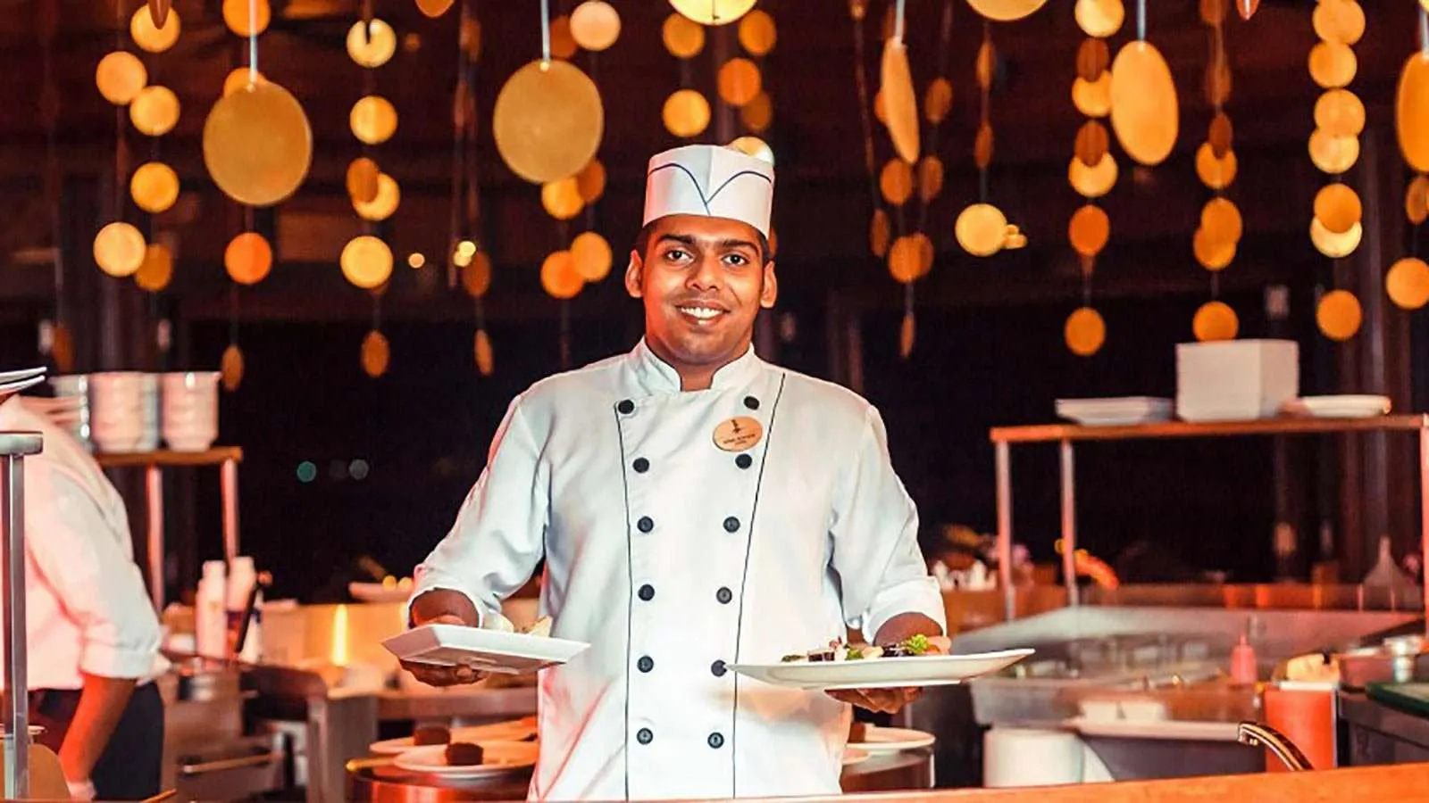 A Tamarind chef holding 2 plates, among the kitchen’s lanterns