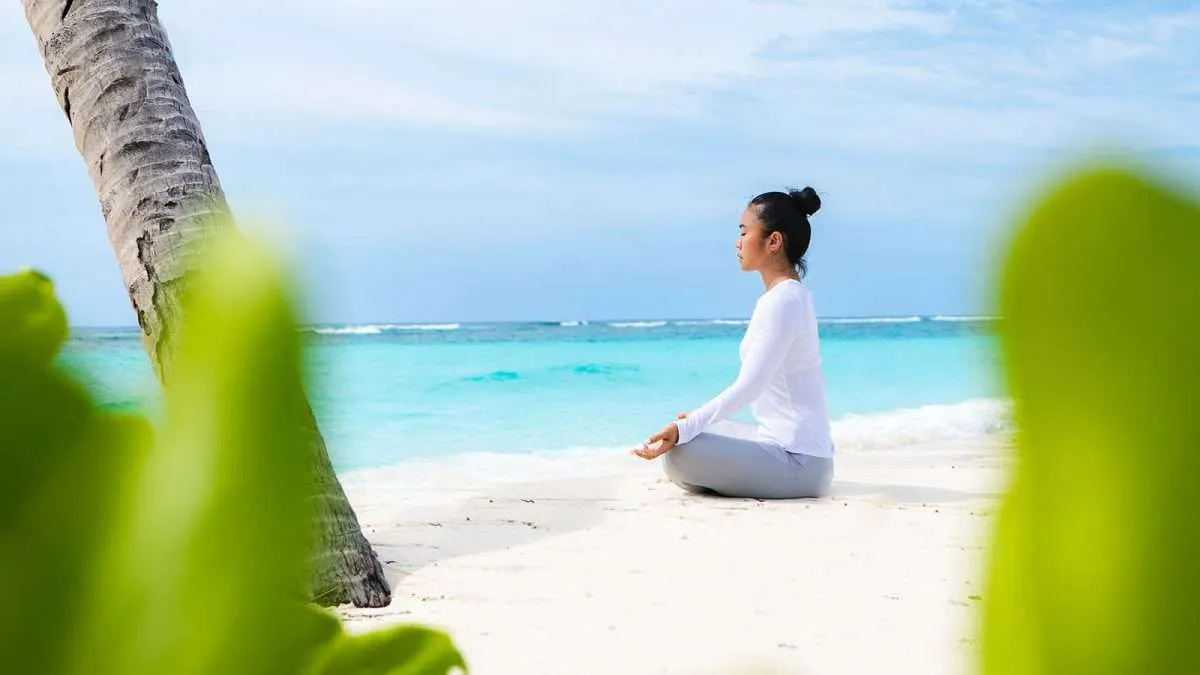 A woman doing yoga on the beach, facing the sea