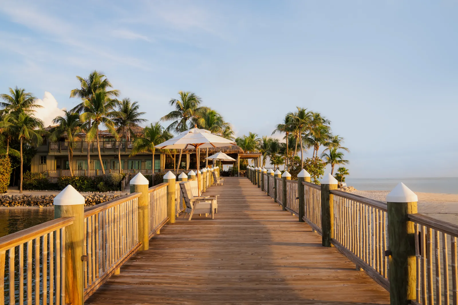 The timber jetty leading to the island, with its railings, a white parasol and the buildings among the palms.