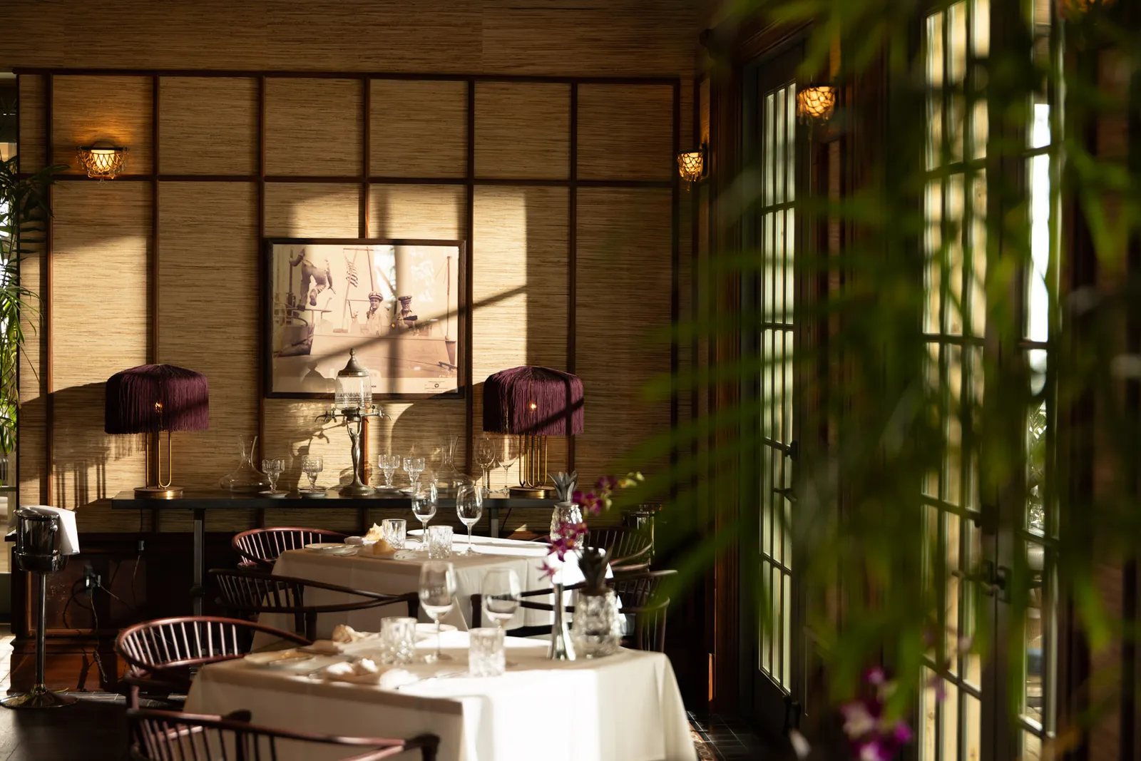 The Dining Room indoors: white-clothed tables, dark-shaded lamps and walls lined with cane.