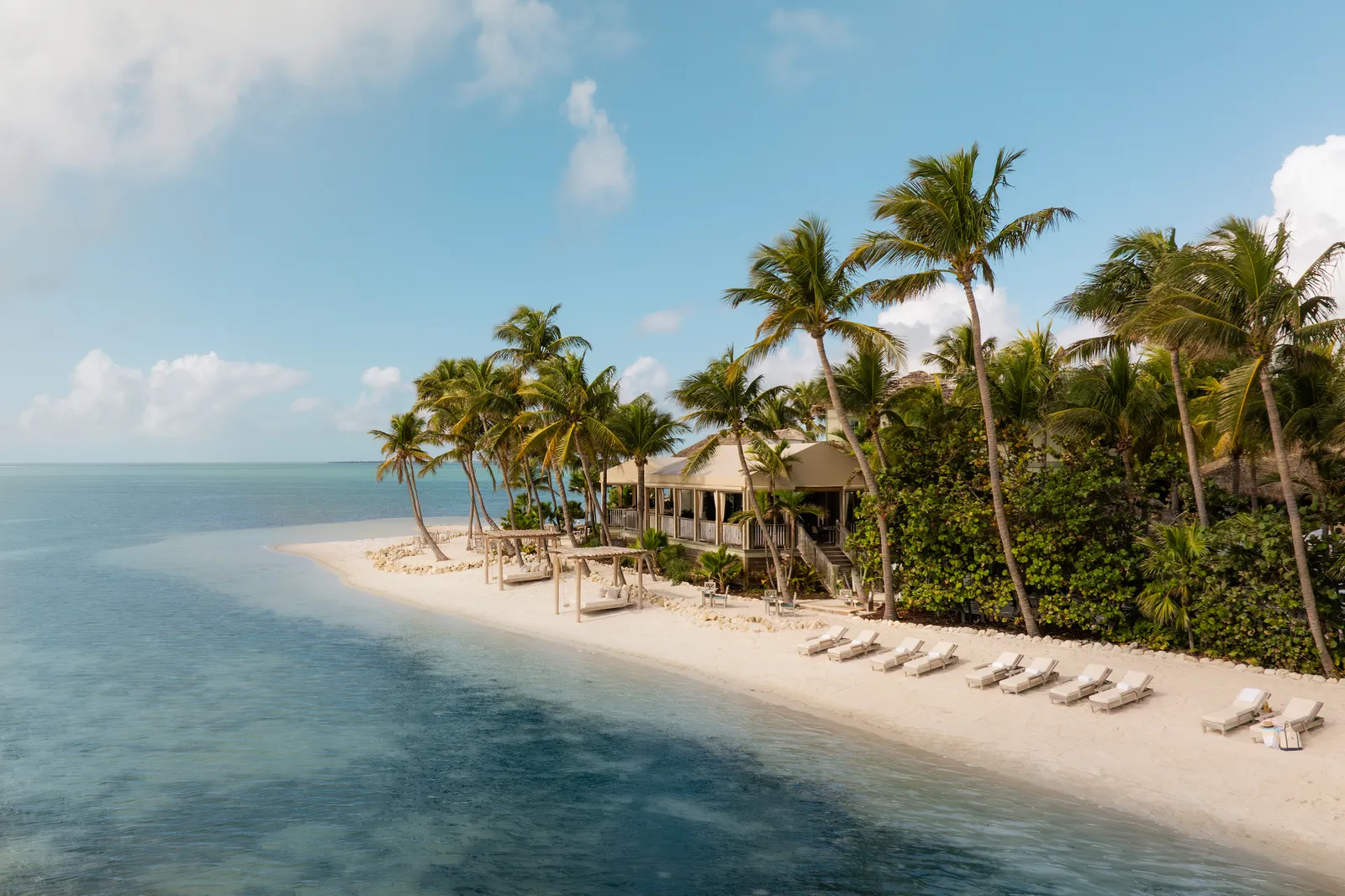 The beach at the island’s tip: pale sand, a row of loungers, coconut palms and a thatched building.