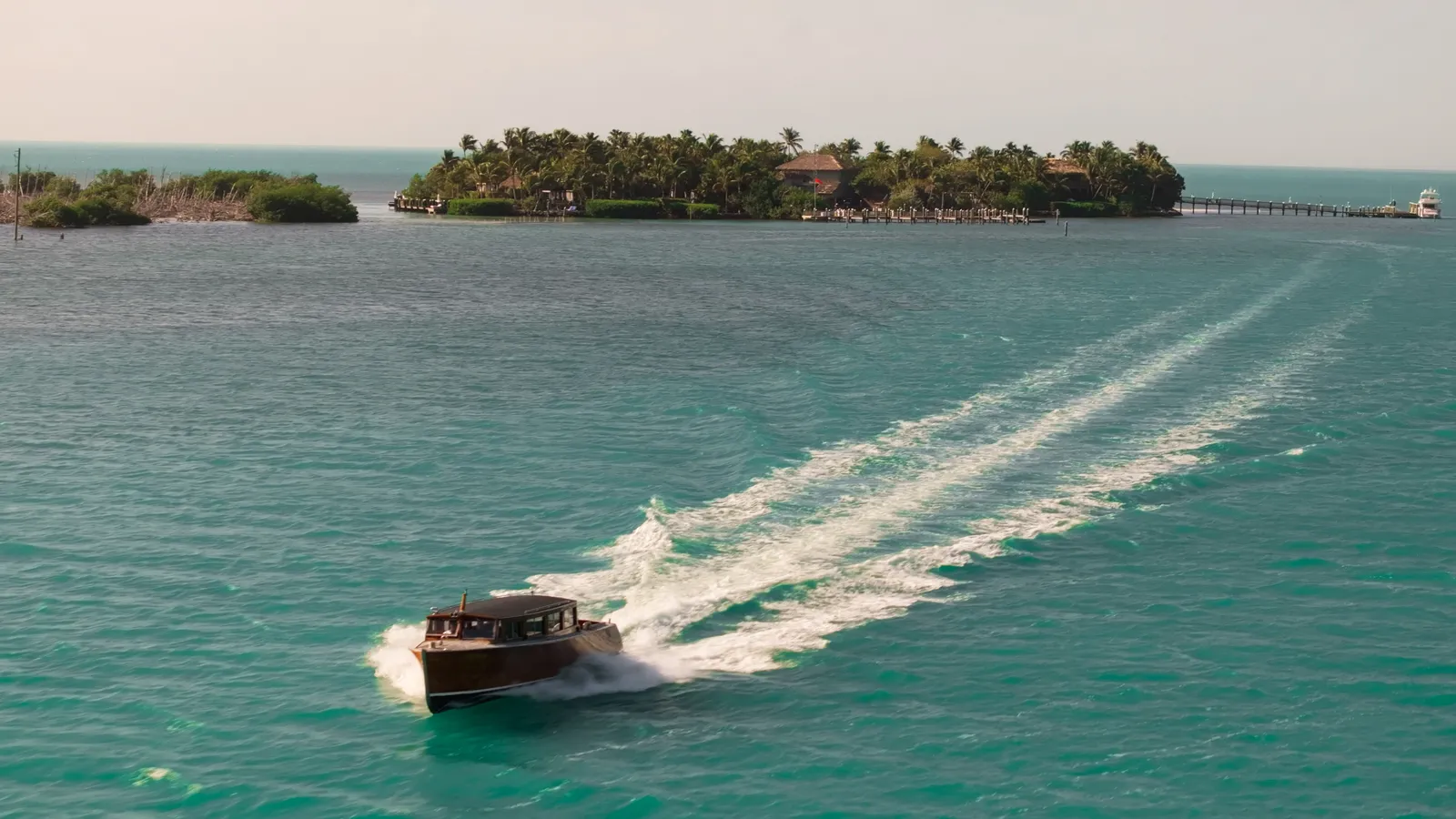 The hotel’s wooden launch at speed over green water, its white wake behind and the palm-covered island beyond.