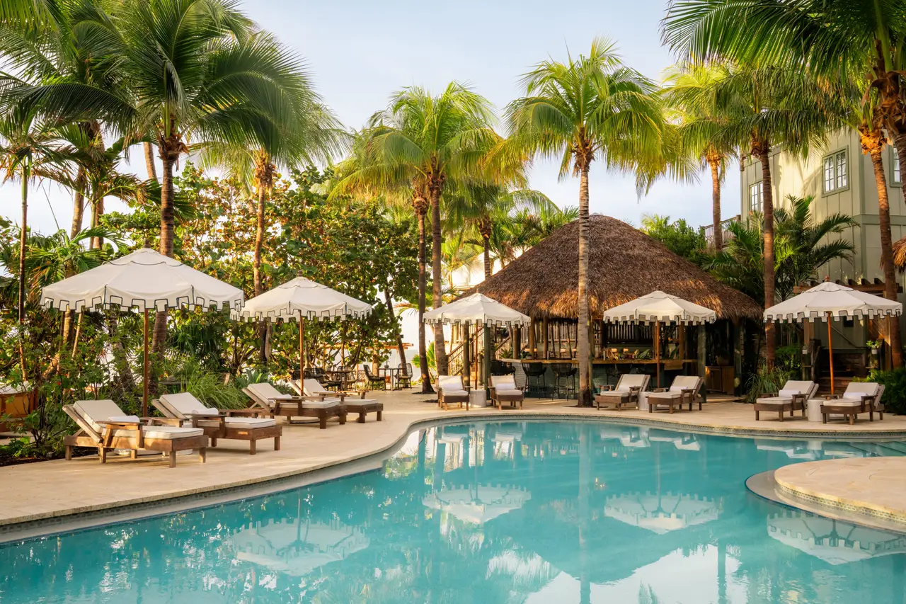 The lagoon pool with the thatched Palapa Bar, white parasols, loungers and coconut palms.