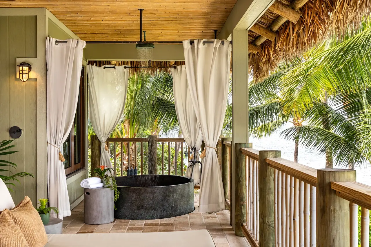 The covered verandah of an upper-floor suite, with its copper tub, white drapes and the palms beyond the rail.