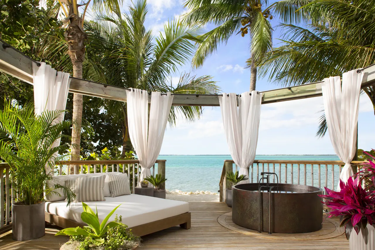 An Island Romance Suite’s deck: the day bed, the copper tub, white drapes and the turquoise sea beyond the rail.