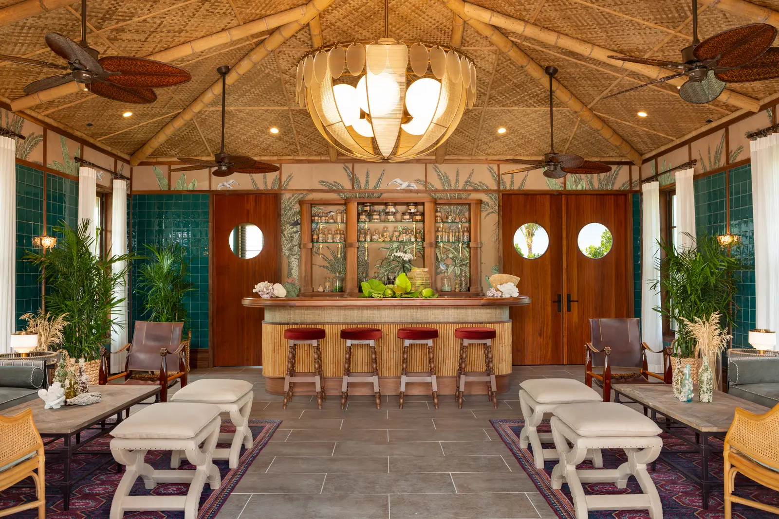 Inside the Shore Station: the bar and its stools, doors with portholes, a chandelier and fans under the thatch.