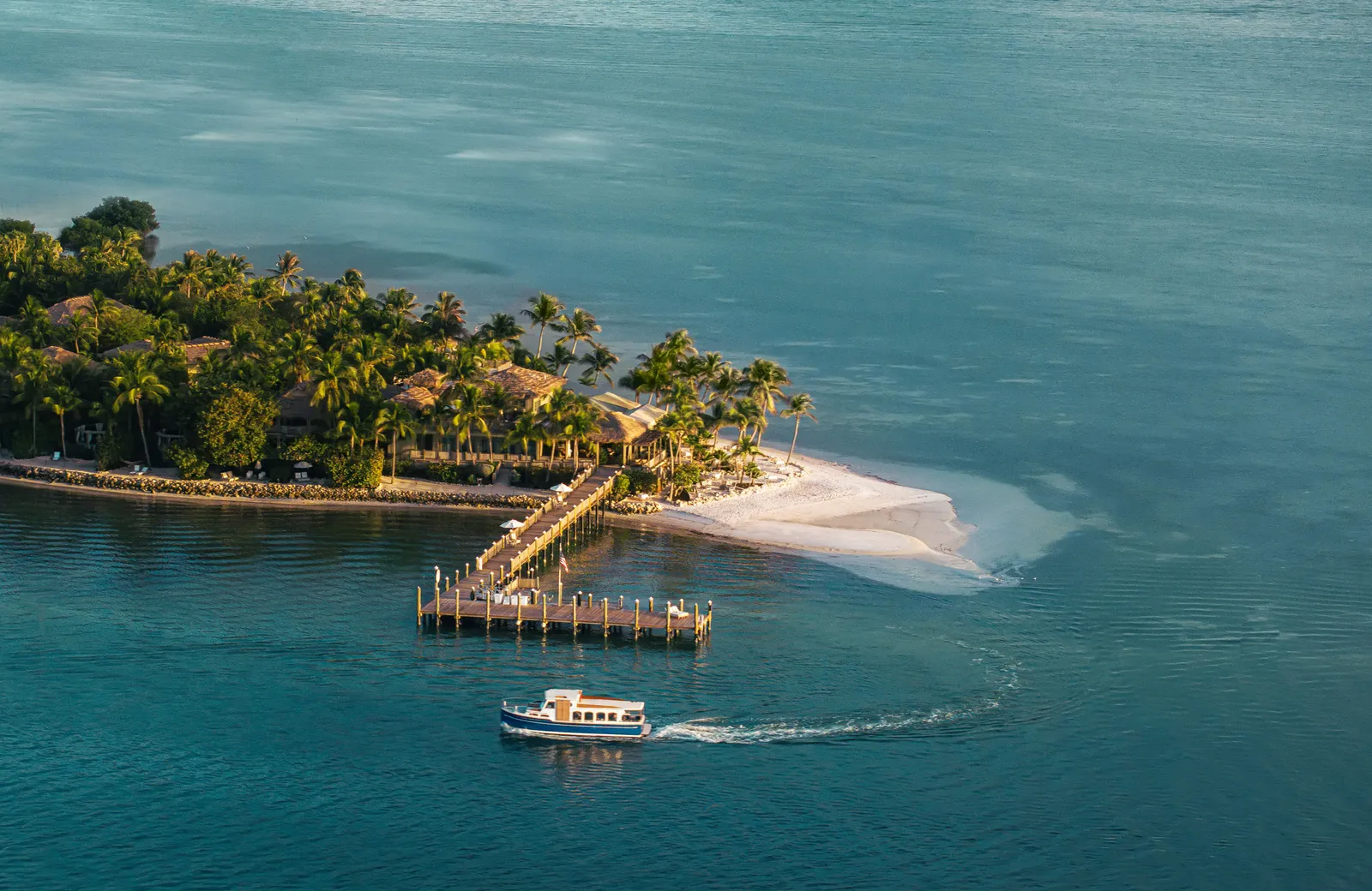 The island from the air, with its jetty, a spit of sand and a boat pulling away in a curving wake.