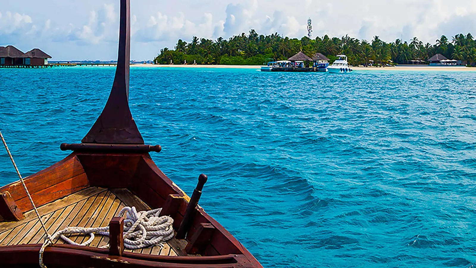 The bow of a dhoni out at sea, with another island in the distance.