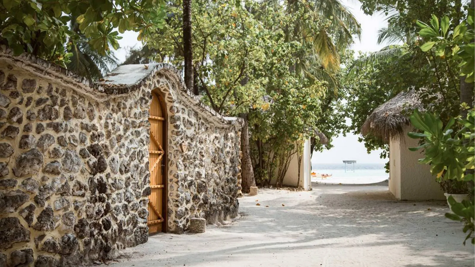 The sandy lane between the Garden Villas’ coral walls, with a wooden door and the sea at the end.