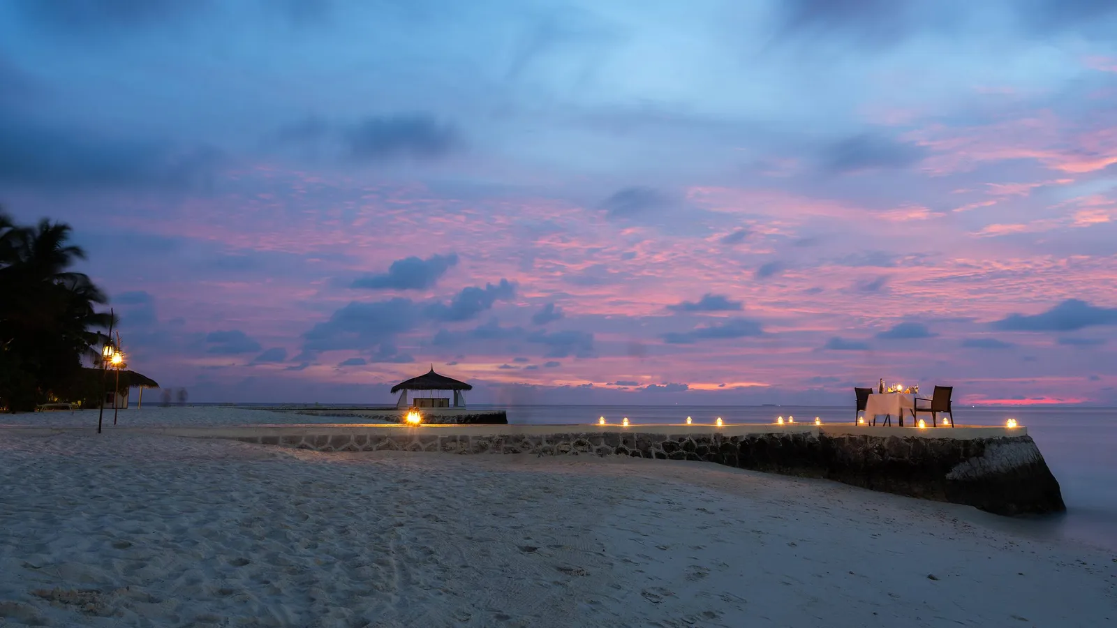 A table laid at the end of the jetty at dusk, with the candles lit.