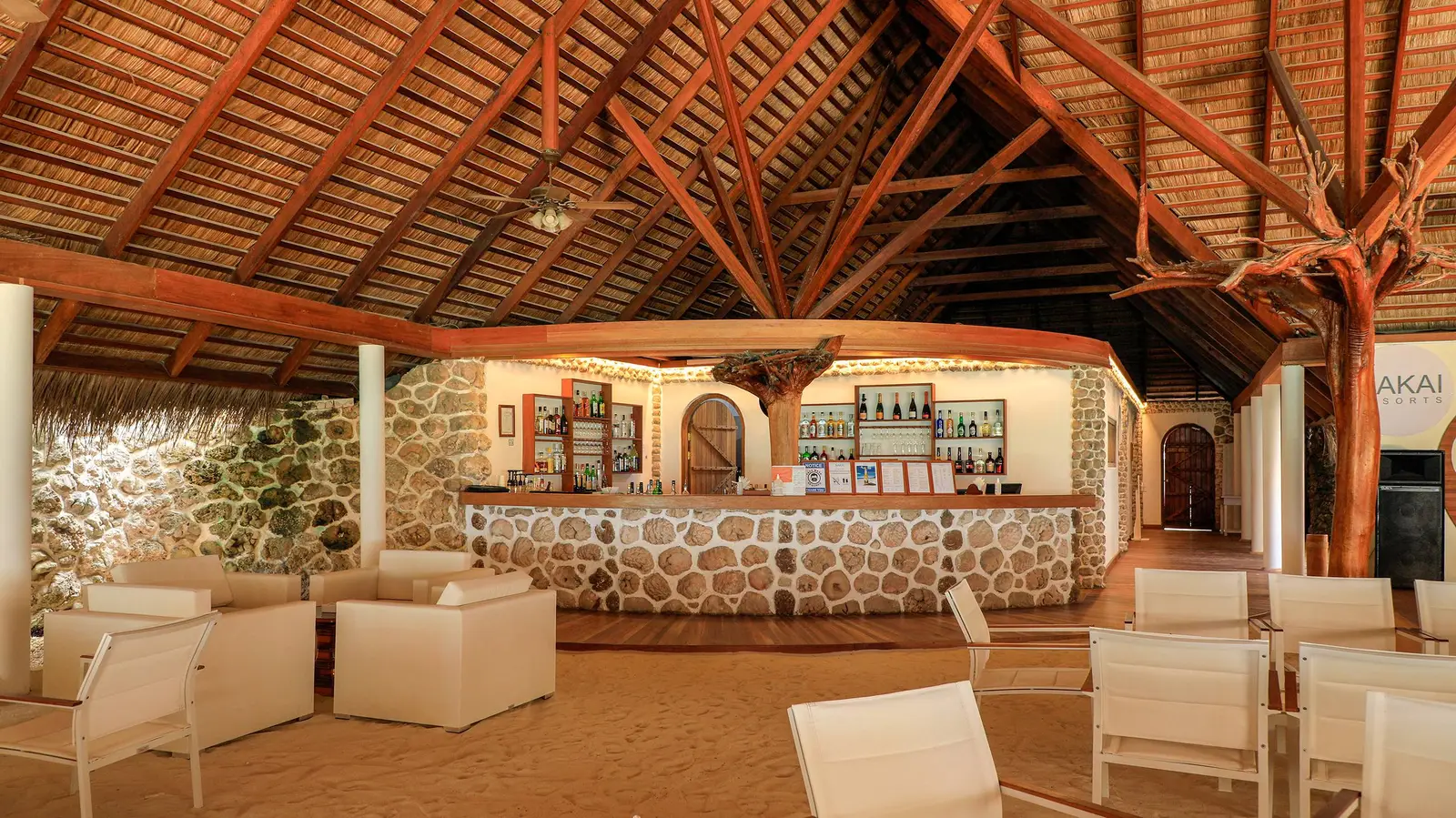 The main bar, with its coral-stone counter and white armchairs under the timber roof.