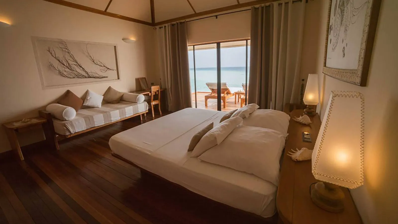 An Over Water bedroom: the bed, the sofa and the glass door open onto the deck and the sea.