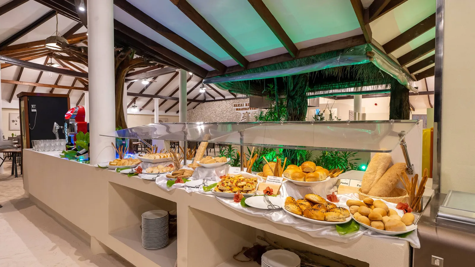 The restaurant buffet under the great timber roof, its tables standing on a sand floor.