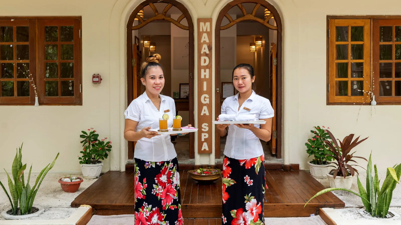 The entrance to the Maadhiga Spa: 2 therapists holding juices and towels before the arched doors.