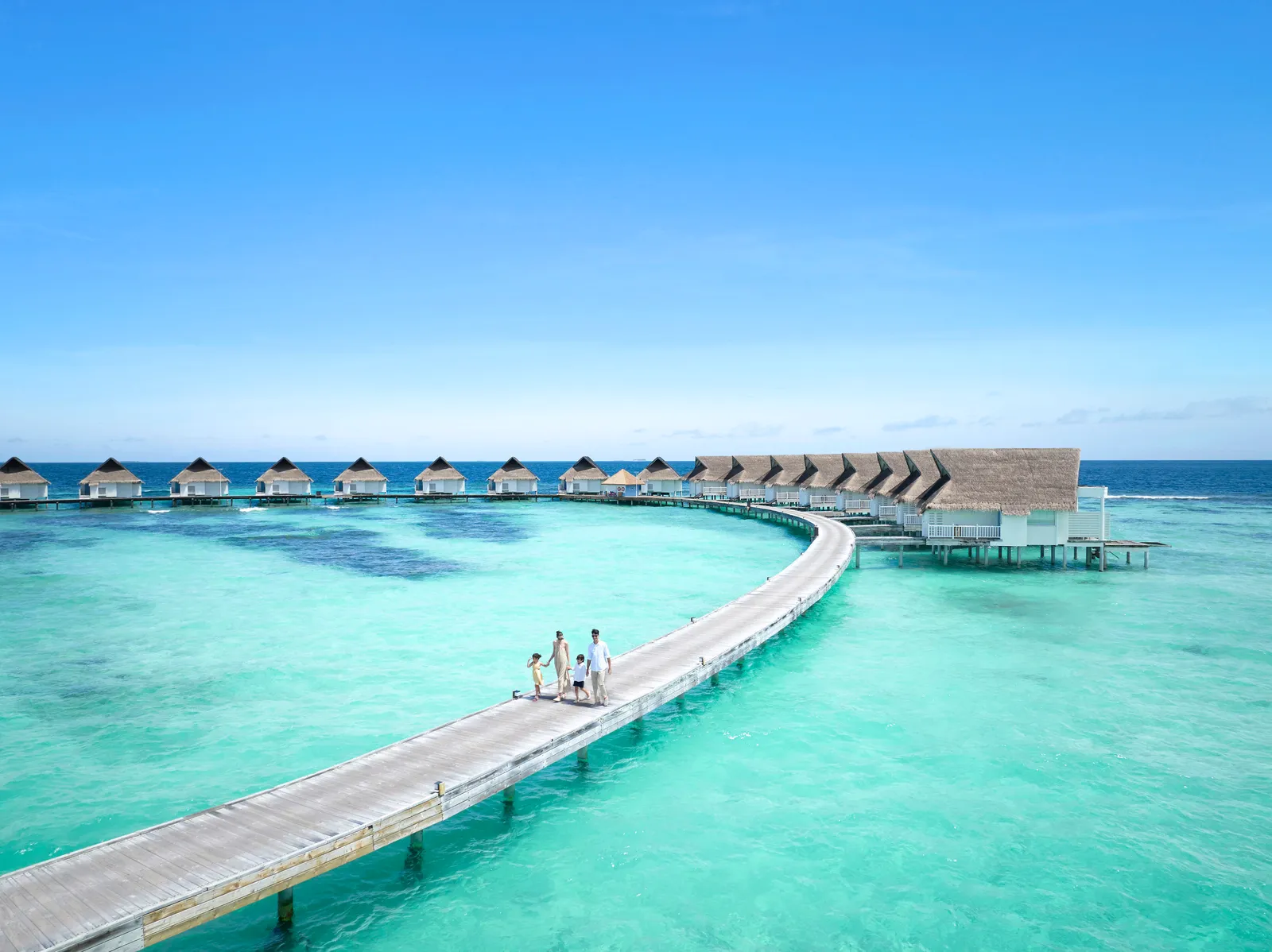 A family walk along the curving jetty to the water villas, over the turquoise lagoon.