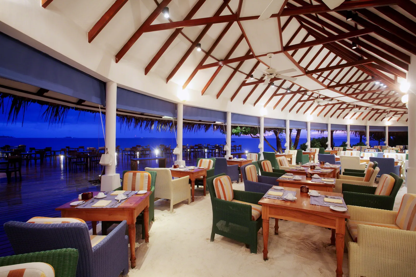 The Reef dining room in the evening, with its sand floor, the laid tables and the timber roof beams.