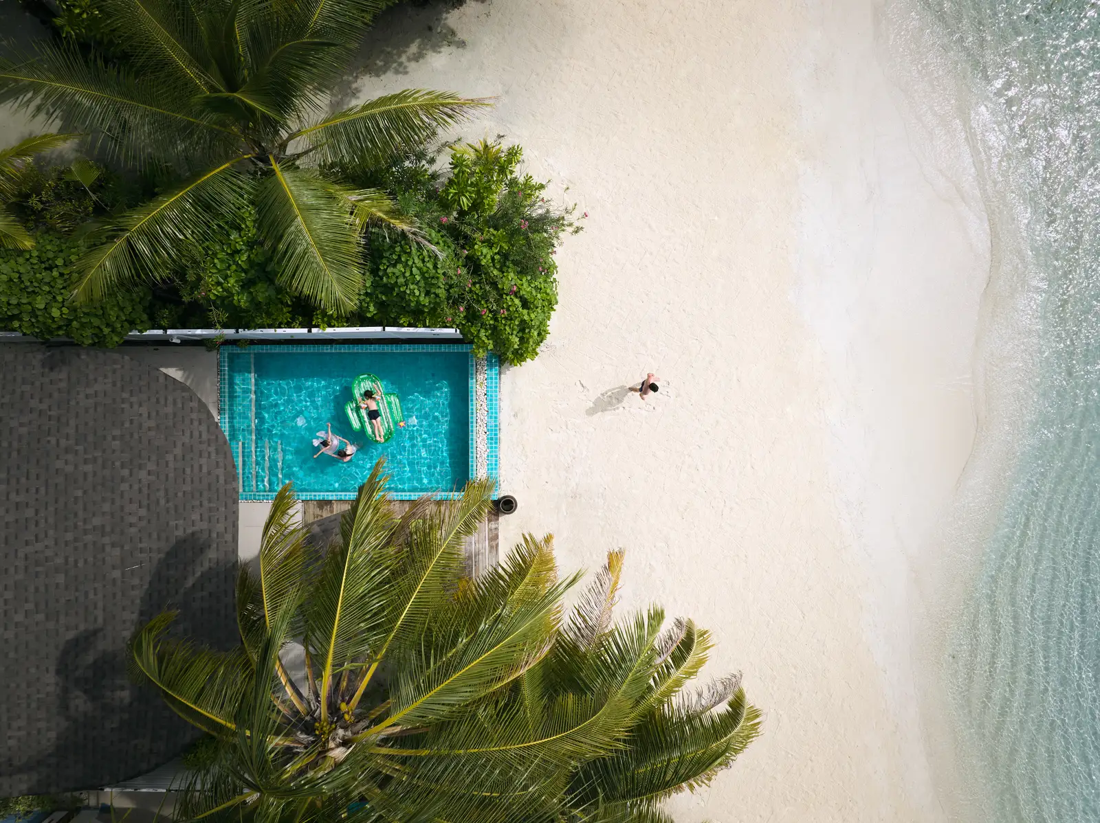 A Club Two Bedroom Beach Pool Villa from above: the private pool between the palms and the white beach, a guest in the water.