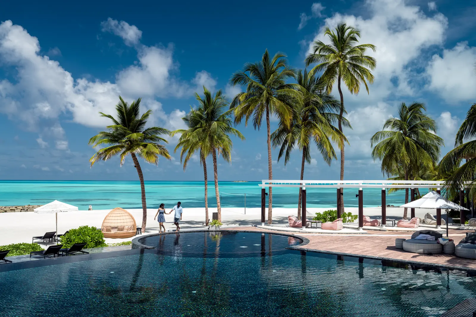 The main pool beside the Splash Bar, with palms, the white beach and the lagoon beyond the loungers.