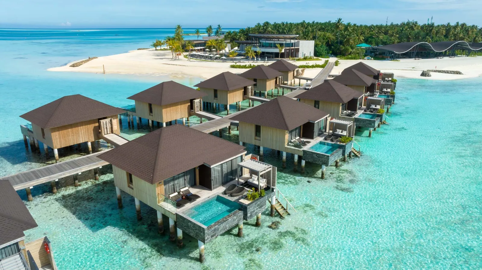 The water villas from above, each with a pool on its deck, and the island and its beach behind.